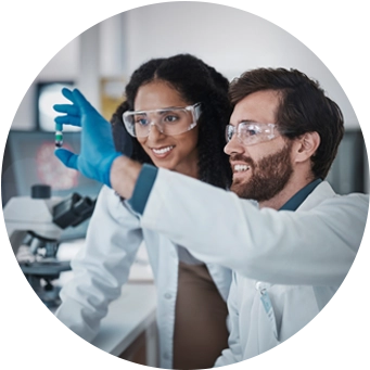 Laboratuvarda güvenlik gözlüğü ve eldiven takan iki bilim insanı, birlikte bir numuneyi analiz ediyor