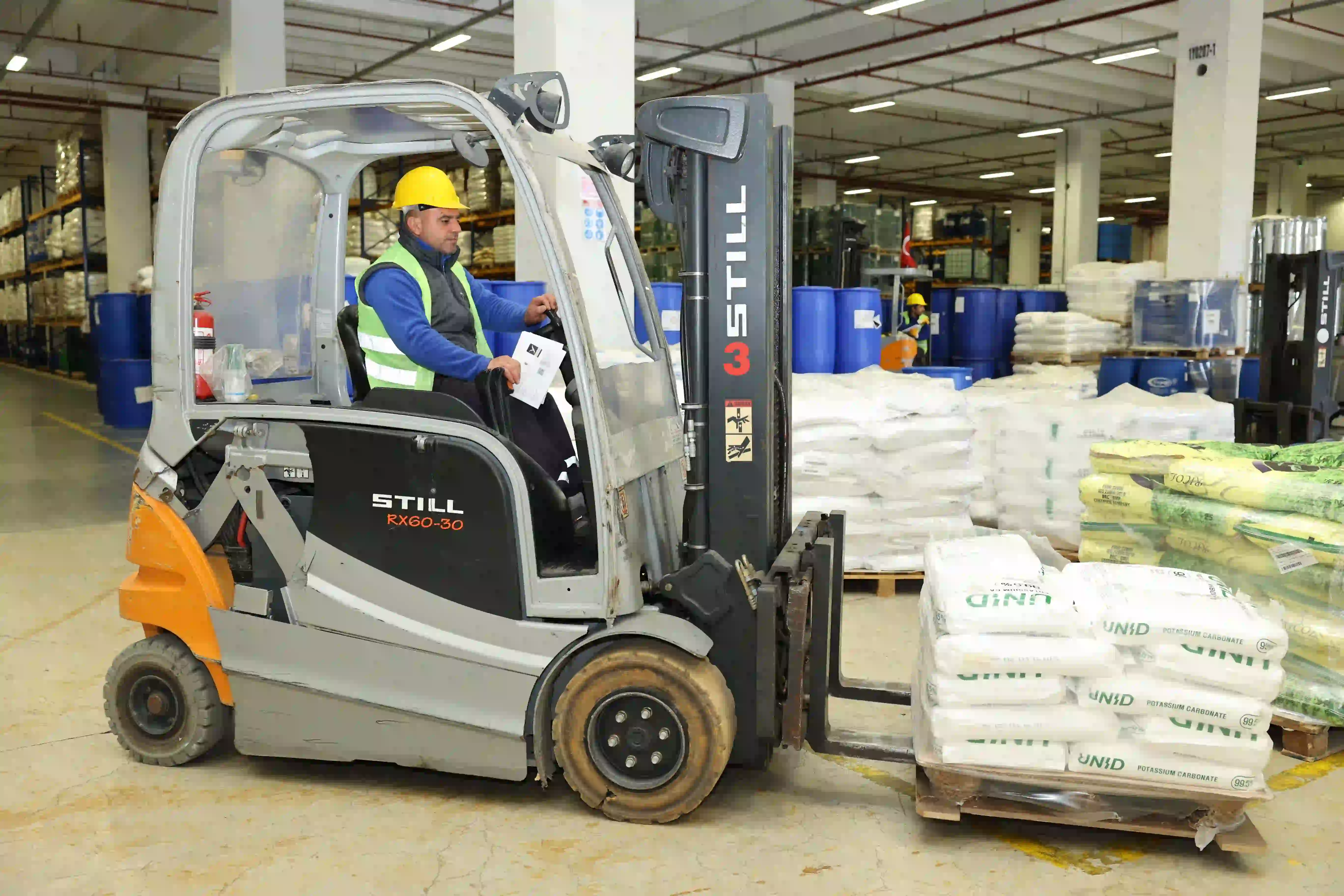 Bir işçi, kimyasal hammaddelerin dağıtımı için depoda forklift kullanıyor.